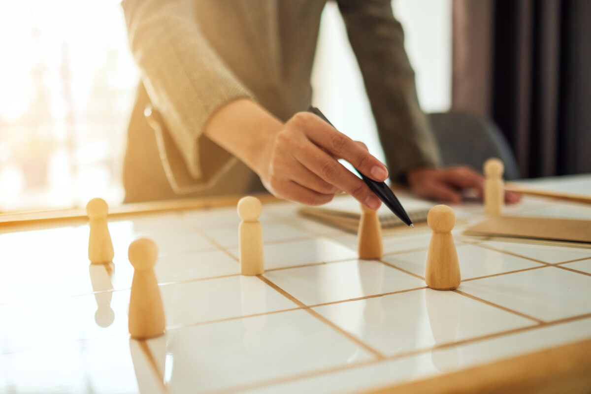 Businesswoman leader choosing and pointing at one of wooden peop Businesswoman leader choosing and pointing at one of wooden people from a group of employees on a planning board